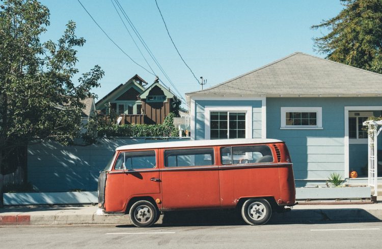 Old, red, vw van outside of a blue house in a neighborhood