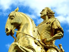 a golden statue of a powerful man riding a horse against a blue and white sky