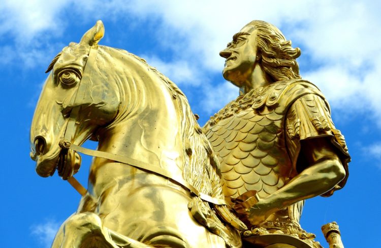 a golden statue of a powerful man riding a horse against a blue and white sky
