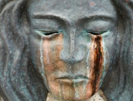 gray sculpture of a woman with closed eyes where the path of tears are brozen and rusted